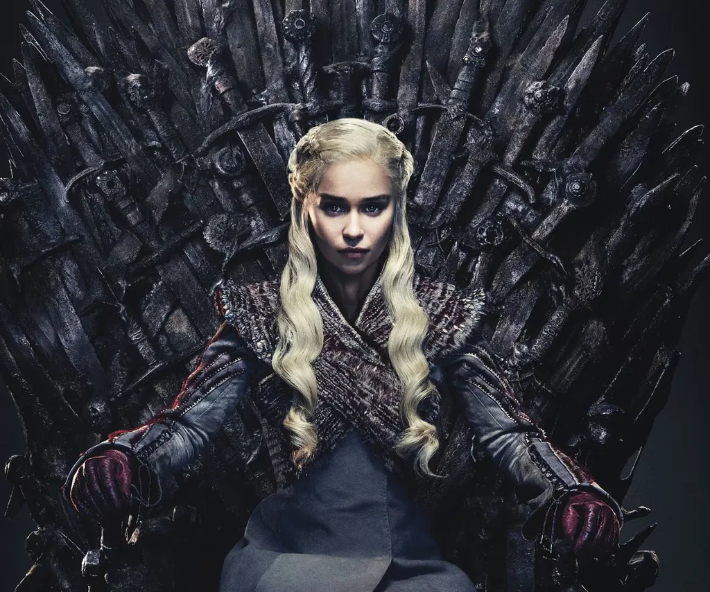 Daenerys Targaryen from Game of Thrones sits on the Iron Throne in dark colours, long wavy blonde hair and a power stare.