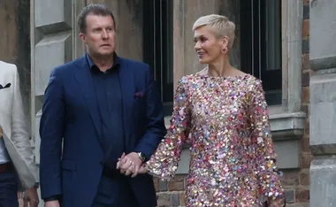 Pete, in a blue suit, and Jess, in a sequin dress, hold hands