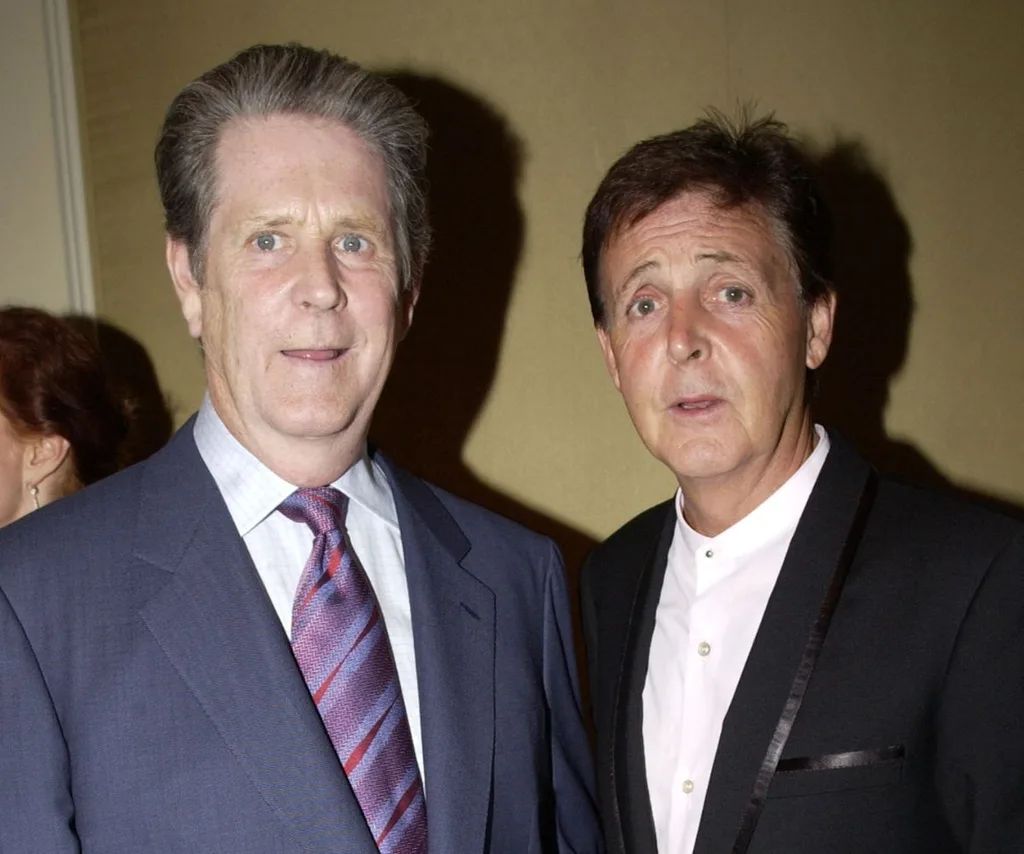 Brian Wilson stands with Paul McCartney, looking at camera, both in suits