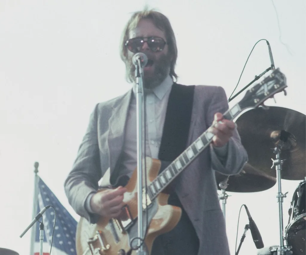 Carl Wilson plays guitar, sings, wearing sunglasses outside on stage