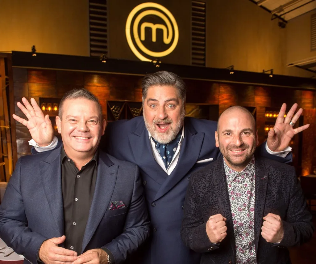 Former MasterChef judges Gary Mehigan, George Calombaris, and Matt Preston smile in front of MasterChef logo wearing suits