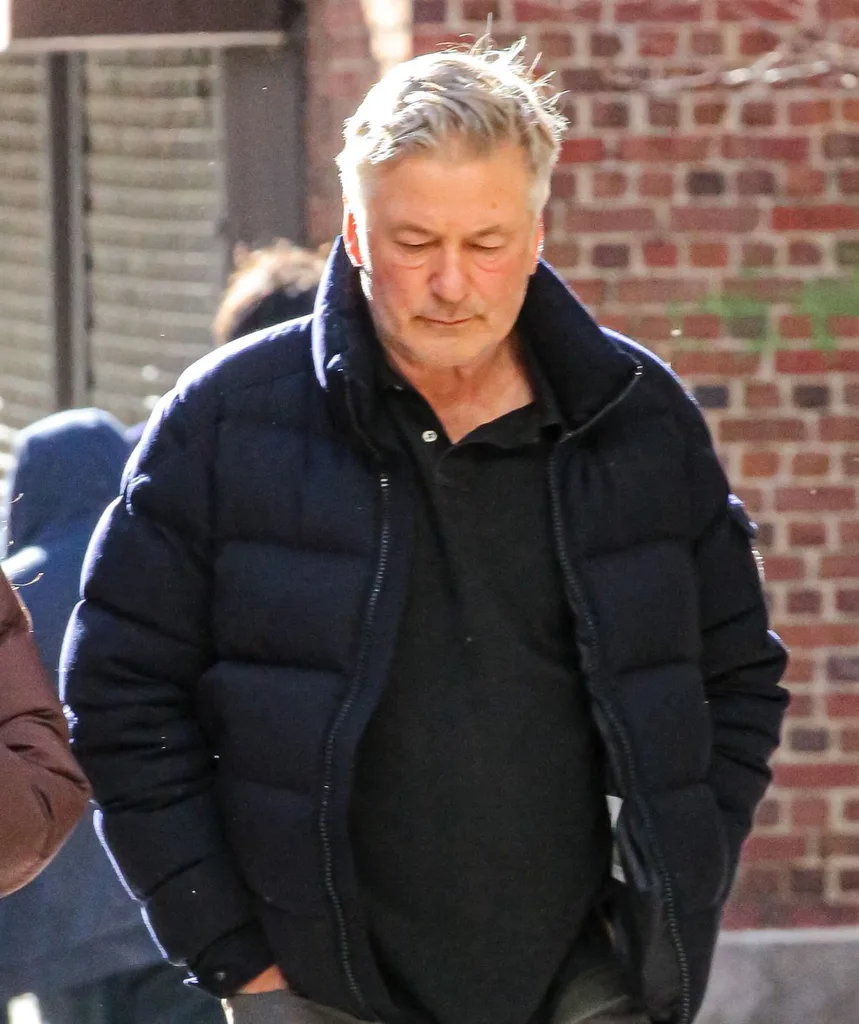 Alec Baldwin outside looking unhappy in a black puffer jacket