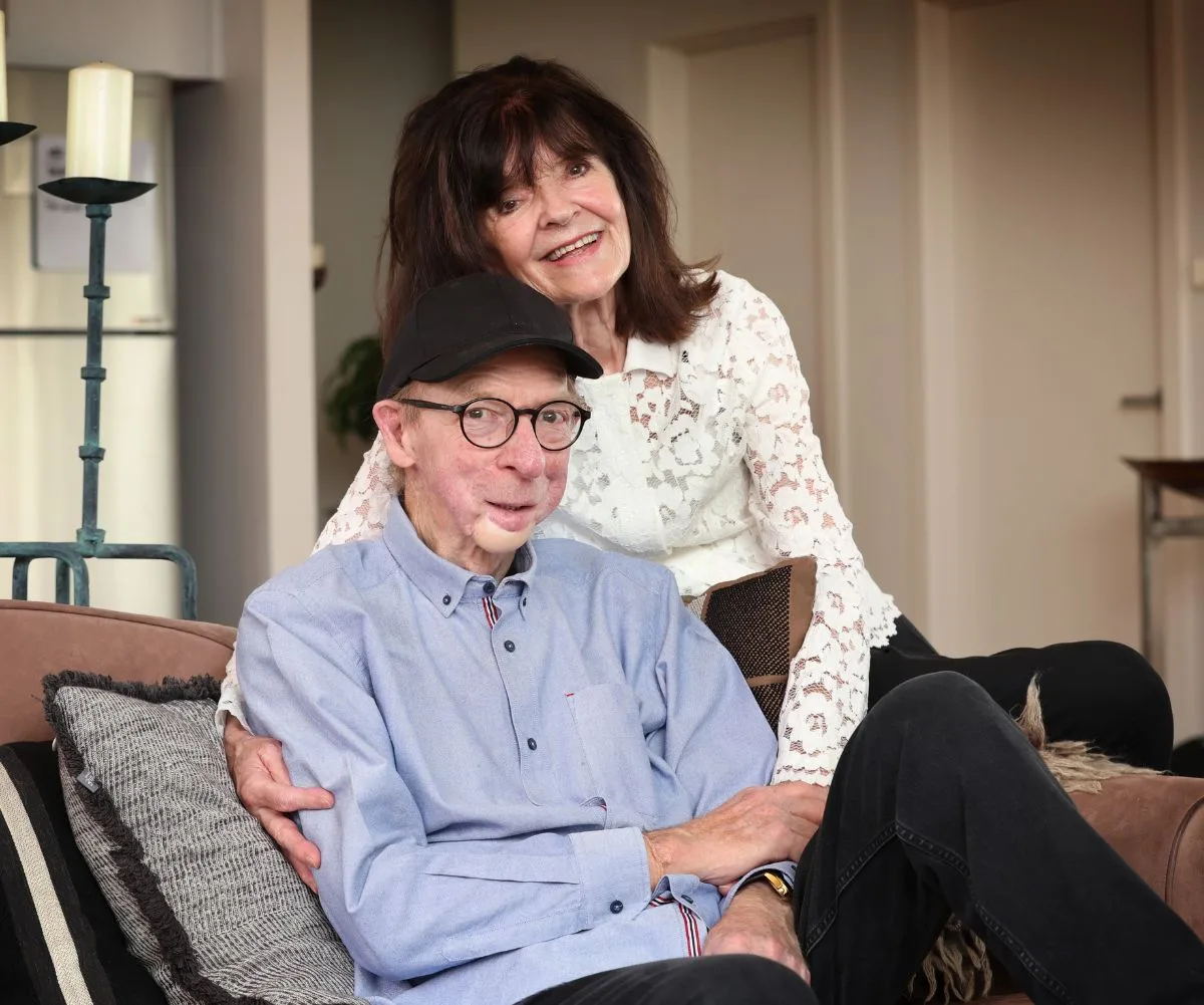 John and his wife Cecile post for a photo in their living room, smiling and embracing each other