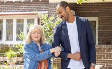 Denise Scott on Mother and Son smiling in denim jacket with arm hooked in cast member's arm