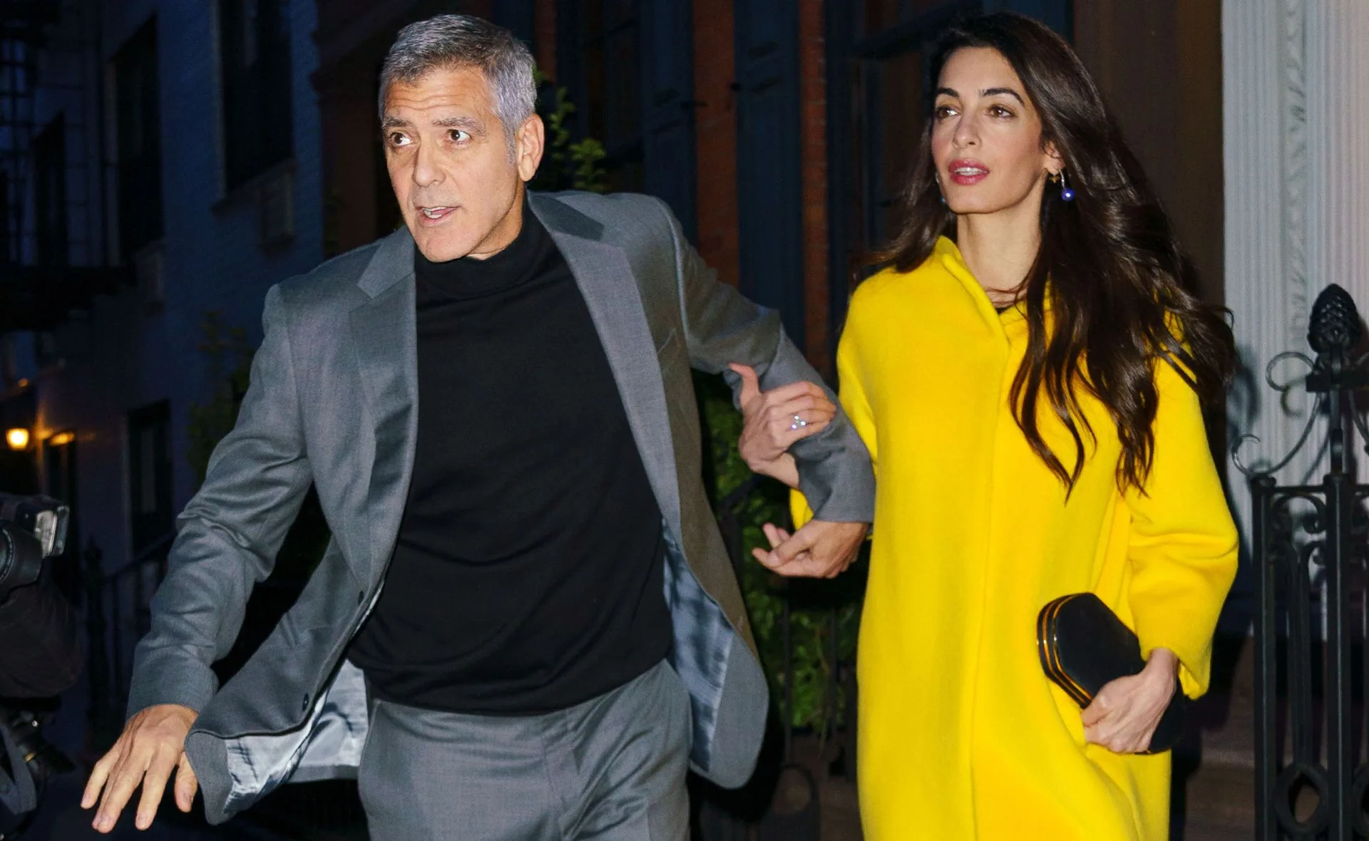 George Clooney, wearing gray suit with black shirt walks with Amal, wearing a vibrant yellow dress