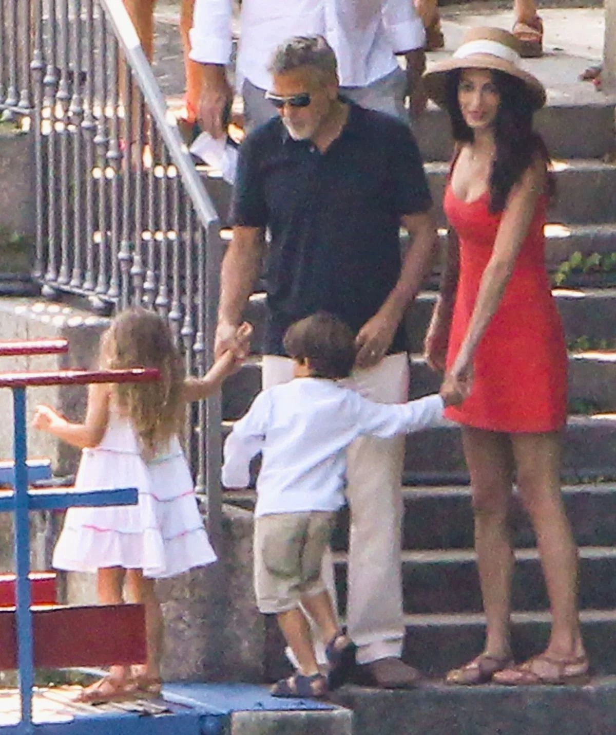 George Clooney and wife Amal holding their twins hands outside on a stair case