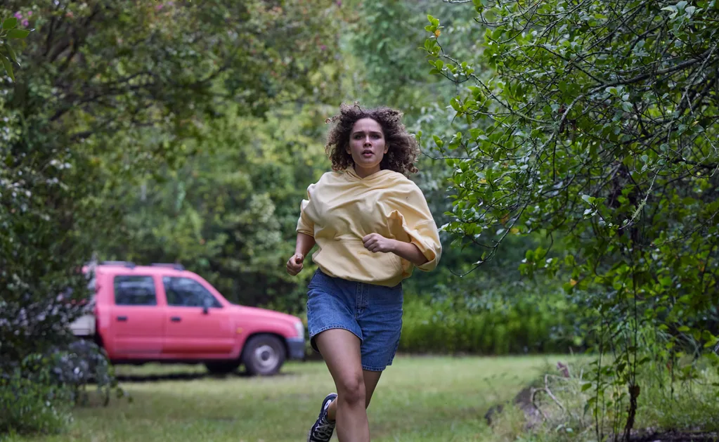 Dana is pictured running from her captor wearing a yellow jumper and blue shorts with a red car in the background.