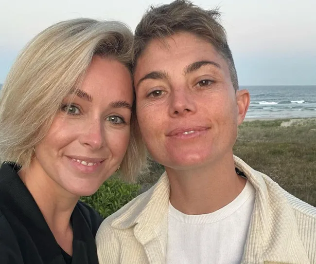 Two people smiling at the camera with the ocean in the background.