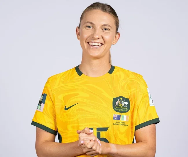 Smiling soccer player in yellow Australian team jersey with hands clasped, logo and number visible.