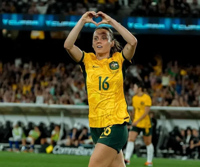 Soccer player in yellow jersey makes heart gesture above head in stadium. Player number 16.