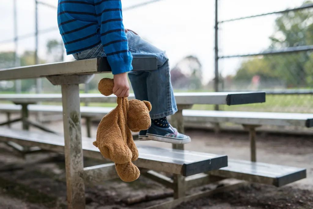 child sitting on a bench holding a sad teddy