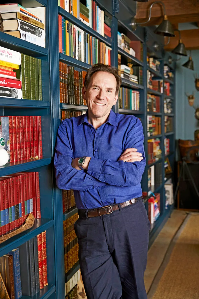 Ben Miller in blue shirt leaning on book case