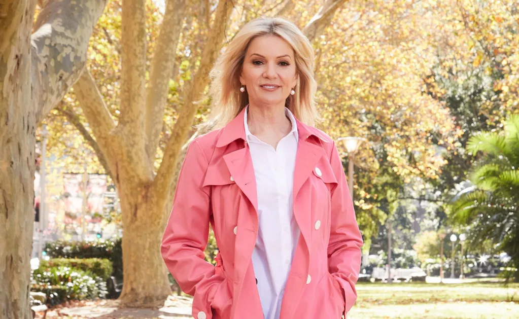 Sandra Sully in pink coat against fall backdrop