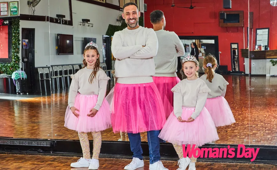 Adam Dovile stans between his daughters, all three in pink tutus and gray sweaters