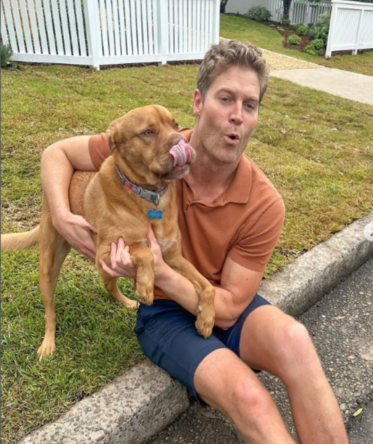 Dr Chris in an orange shirt holding a dog that's licking its lips
