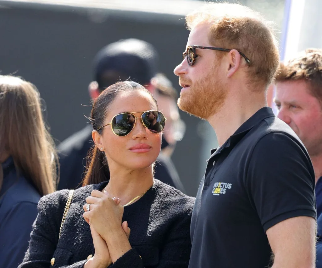 Meghan looks at Harry, both in navy blue.