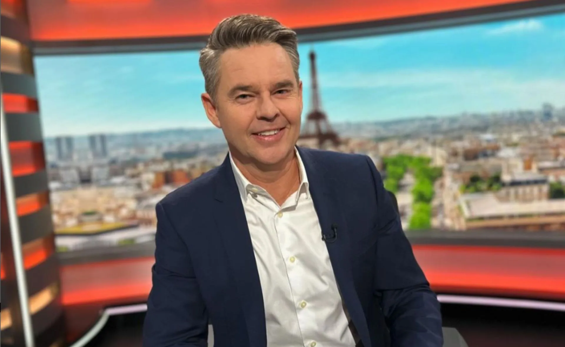 Todd Woodbridge sits at his commentators desk for the Paris Olympics with the Eiffel Tower in the backdrop