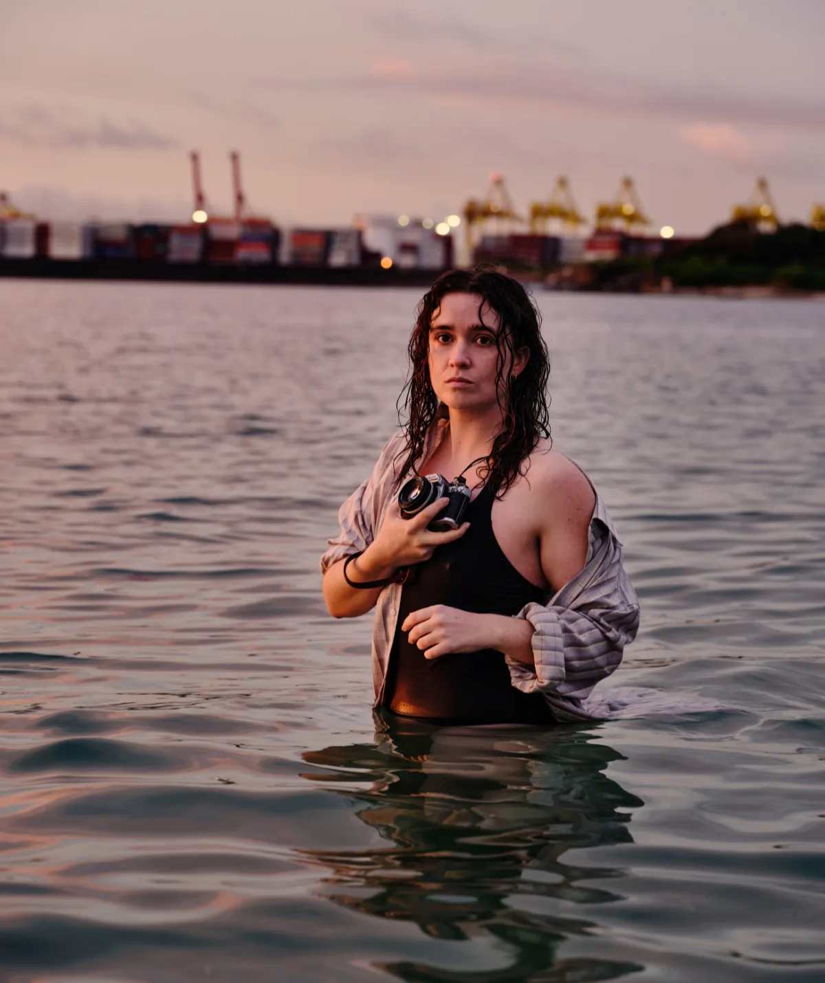 Jacs, played by Alice Englert, is fully clothed in a body of water, cradling a camera.