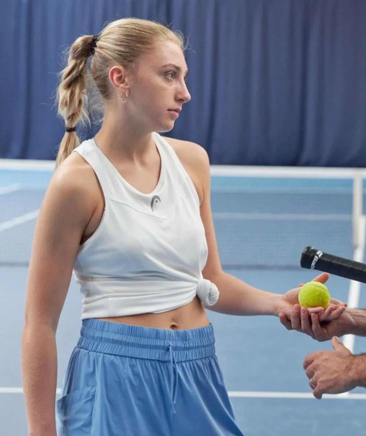 a woman holding a tennis ball on a tennis court looking to the right.
