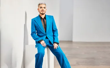 Adam sits on a stool in a two-piece blue suit.