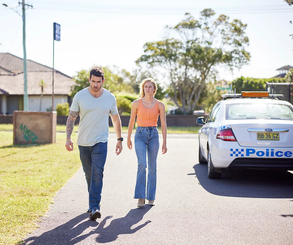 Cash and Felicity walking down the street with a police car on the right