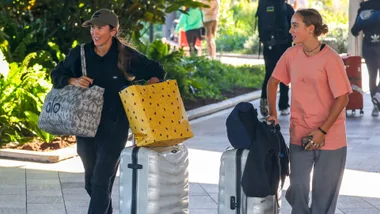 Bec Hewitt pulls her luggage wearing a ball cap