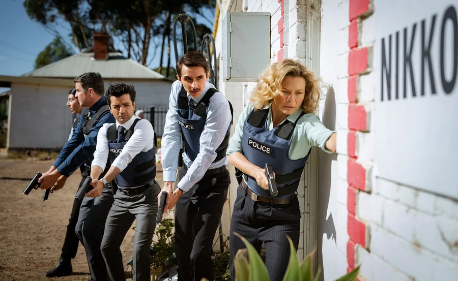 A group of cops with guns, led by Detective Holly O'Rourke (Leeanna Walsman), make their way through a rural property.