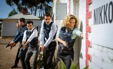 A group of cops with guns, led by Detective Holly O'Rourke (Leeanna Walsman), make their way through a rural property.