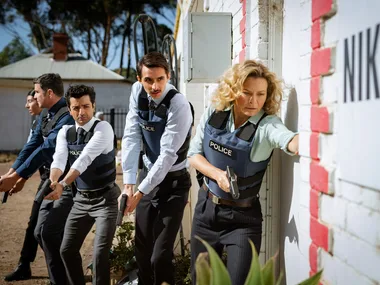 A group of cops with guns, led by Detective Holly O'Rourke (Leeanna Walsman), make their way through a rural property.