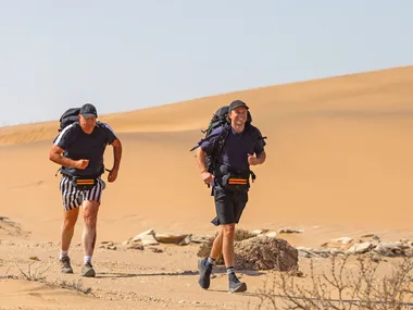 Billy and Oscar Brownless, with backpacks on, are running through sand dunes on The Amazing Race Australia: Celebrity Edition.