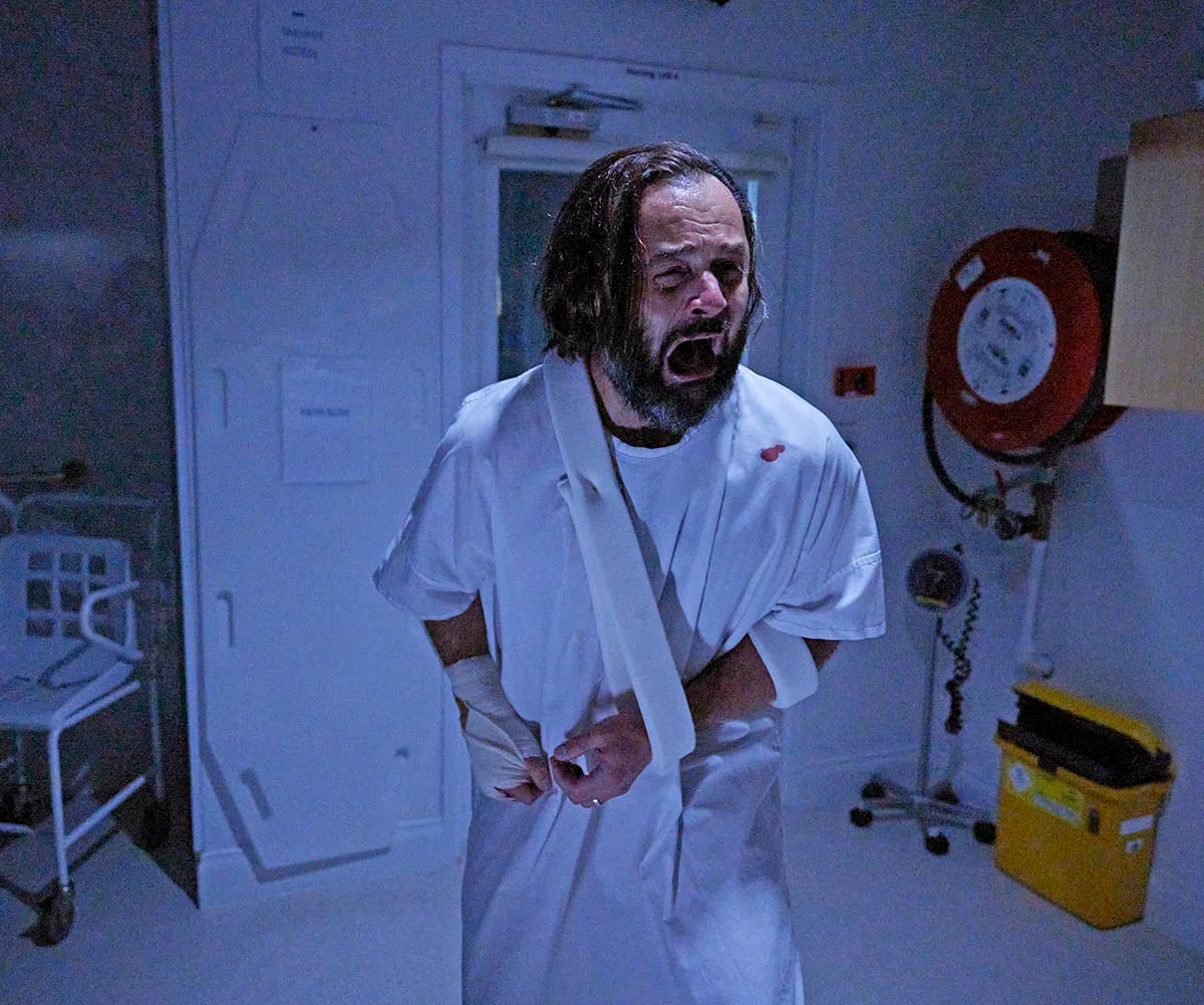 Allan (Gyton Grantley), bandaged and dressed in a hospital gown, screams in terror as he stands in his hospital ward.