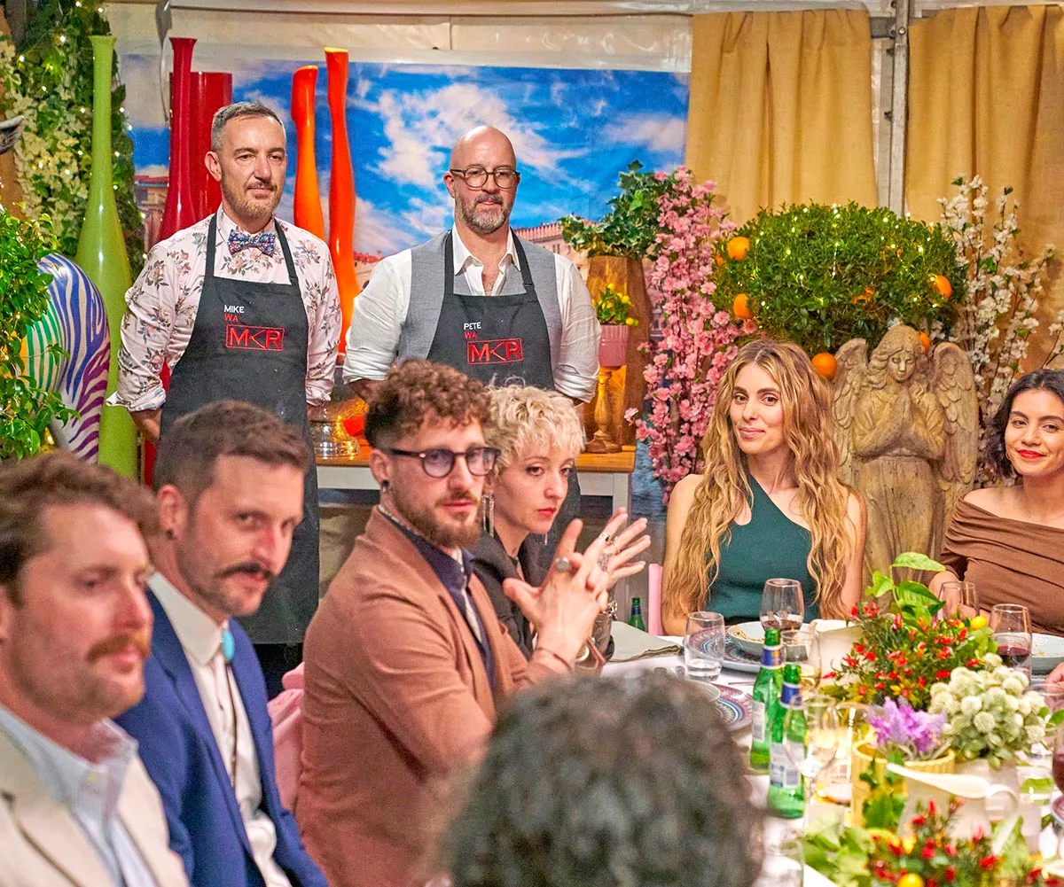 Mike and Pete stand near the dinner table at their instant restaurant. Other teams can be seen sitting around the table.