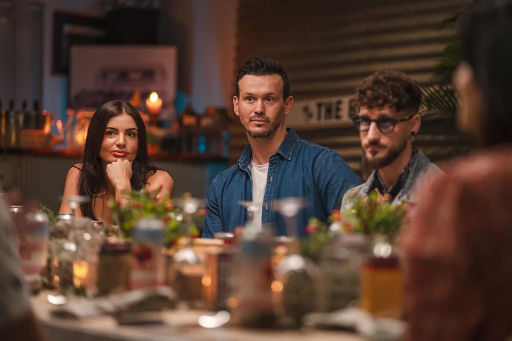 Hannah and Lawrence, sitting next to Simone, listen to another guest talking at an instant restaurant.