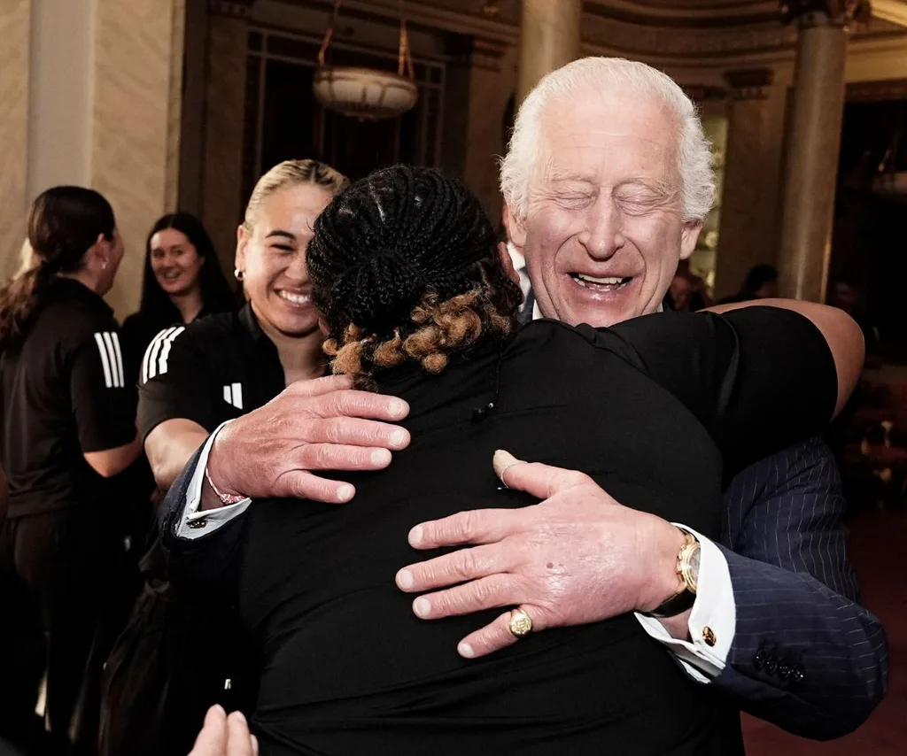 King Charles smiles, eyes closed, as he hugs a NZ Black Fern ruby player