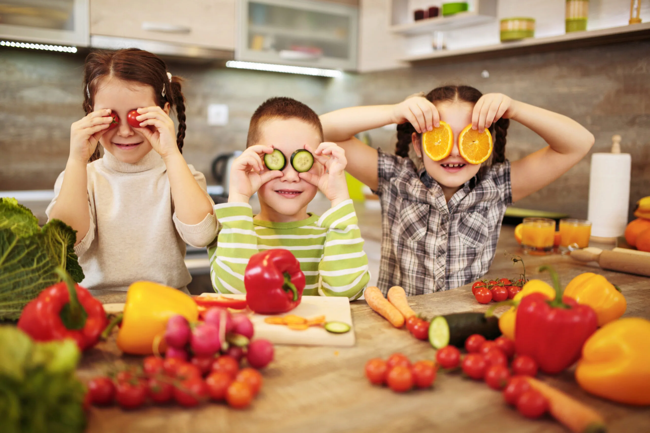 Three small children holding veggies over their eyes