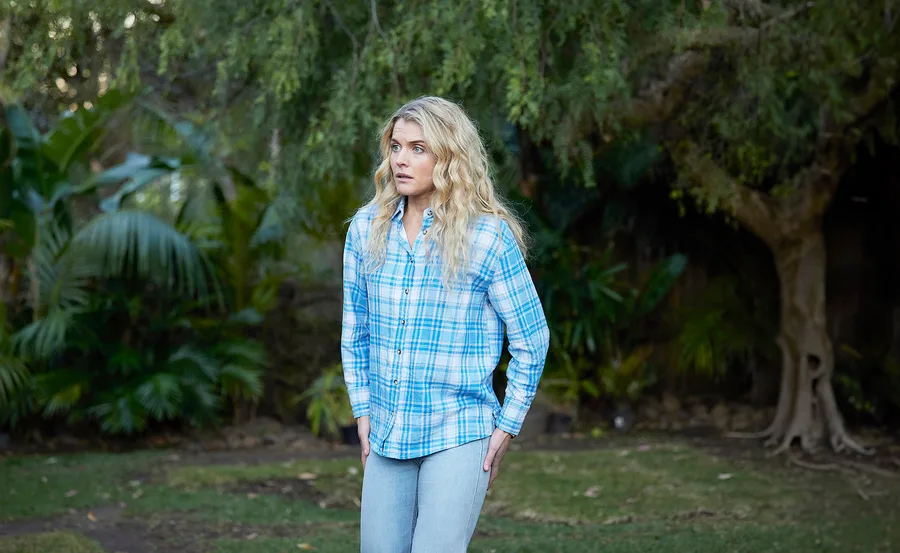 Bree stands in a blue flannelette shirt in a still from Home And Away