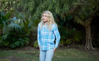 Bree stands in a blue flannelette shirt in a still from Home And Away