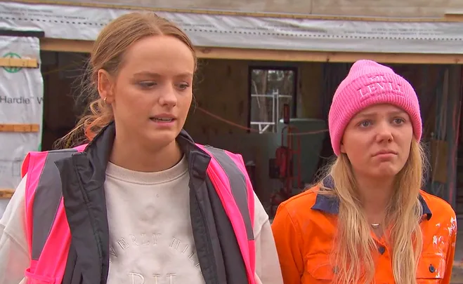 Maddy in pink hi vis and Charlotte in orange hi vis and a pink beanie crying on site while talking to camera