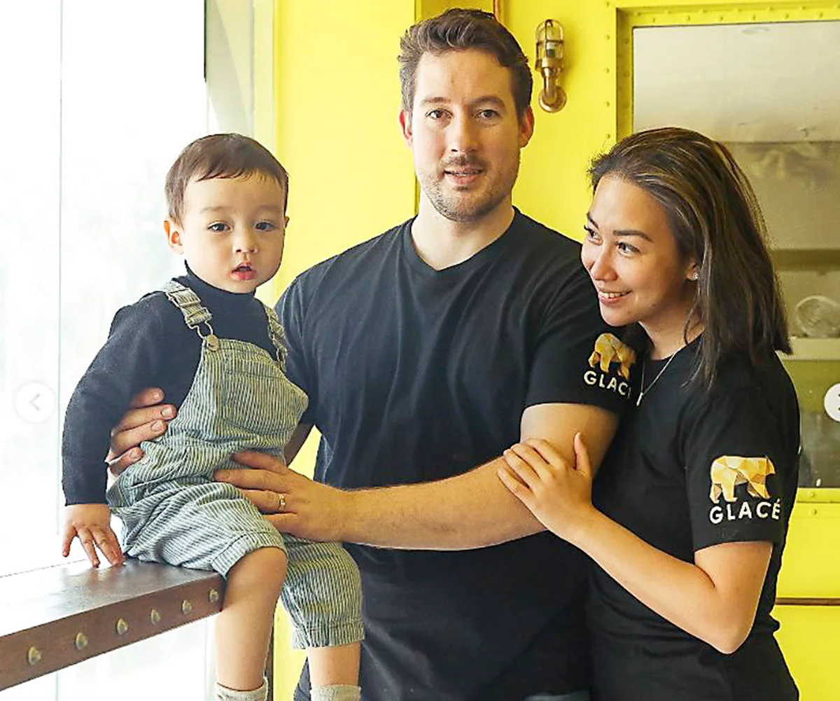 Christy Tania is holding the arm of her husband Luke Johnson, who is holding their son Ben, who is sitting on a bench.