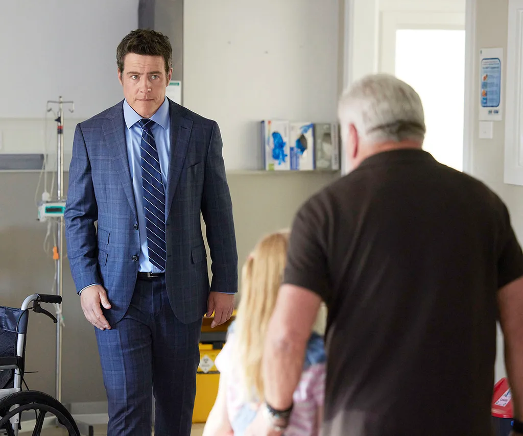 Stephen Peacocke, as Dylan, is wearing a suit while visiting the hospital.