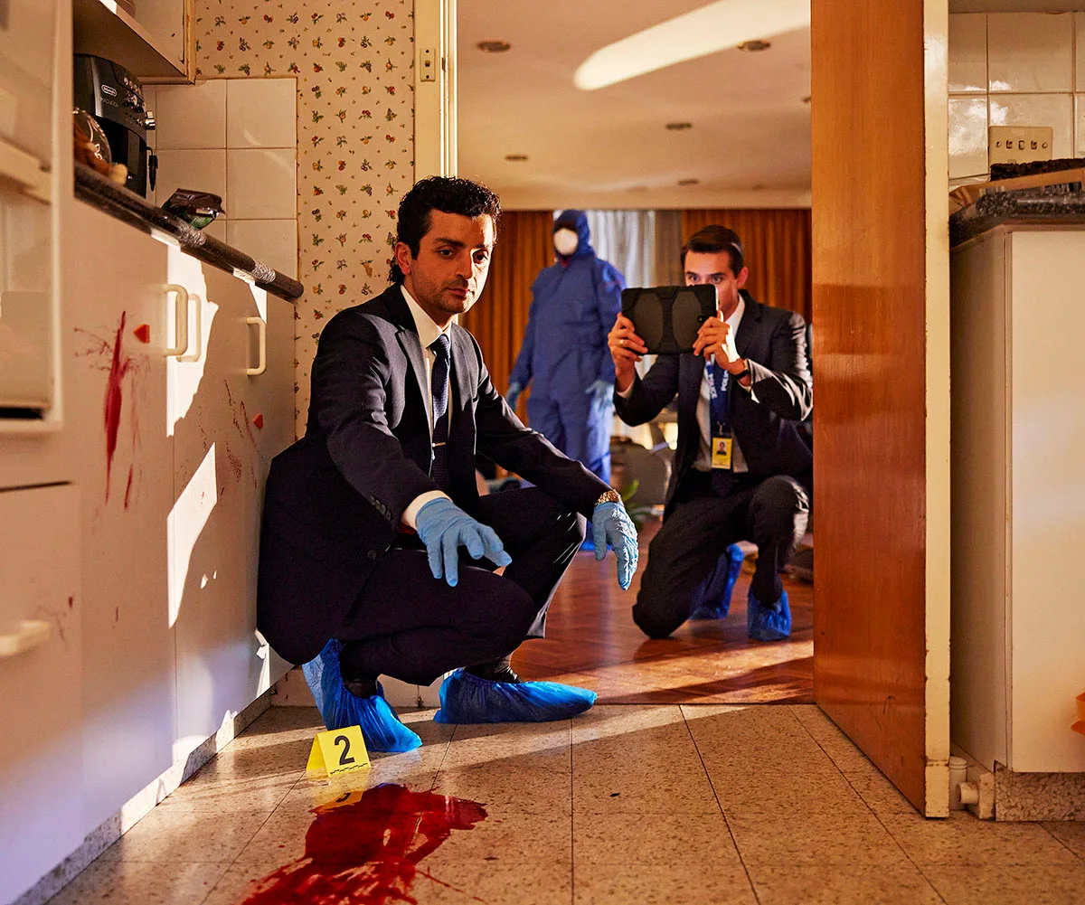 Rahel Romahn, as Jarred, squats near a bloodstain on the floor of a house where a murder has taken place. 