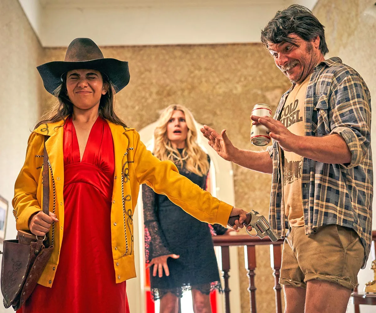 Sherry-Lee Watson, as Robyn, points a gun at the groin of Justin Rosniak, as Steve, while Bonnie Sveen, as Cheryl, stands behind them.