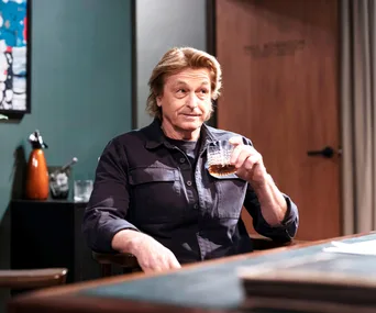 Peter O'Brien, as Shane Ramsay, holds a glass while sitting at a bar.