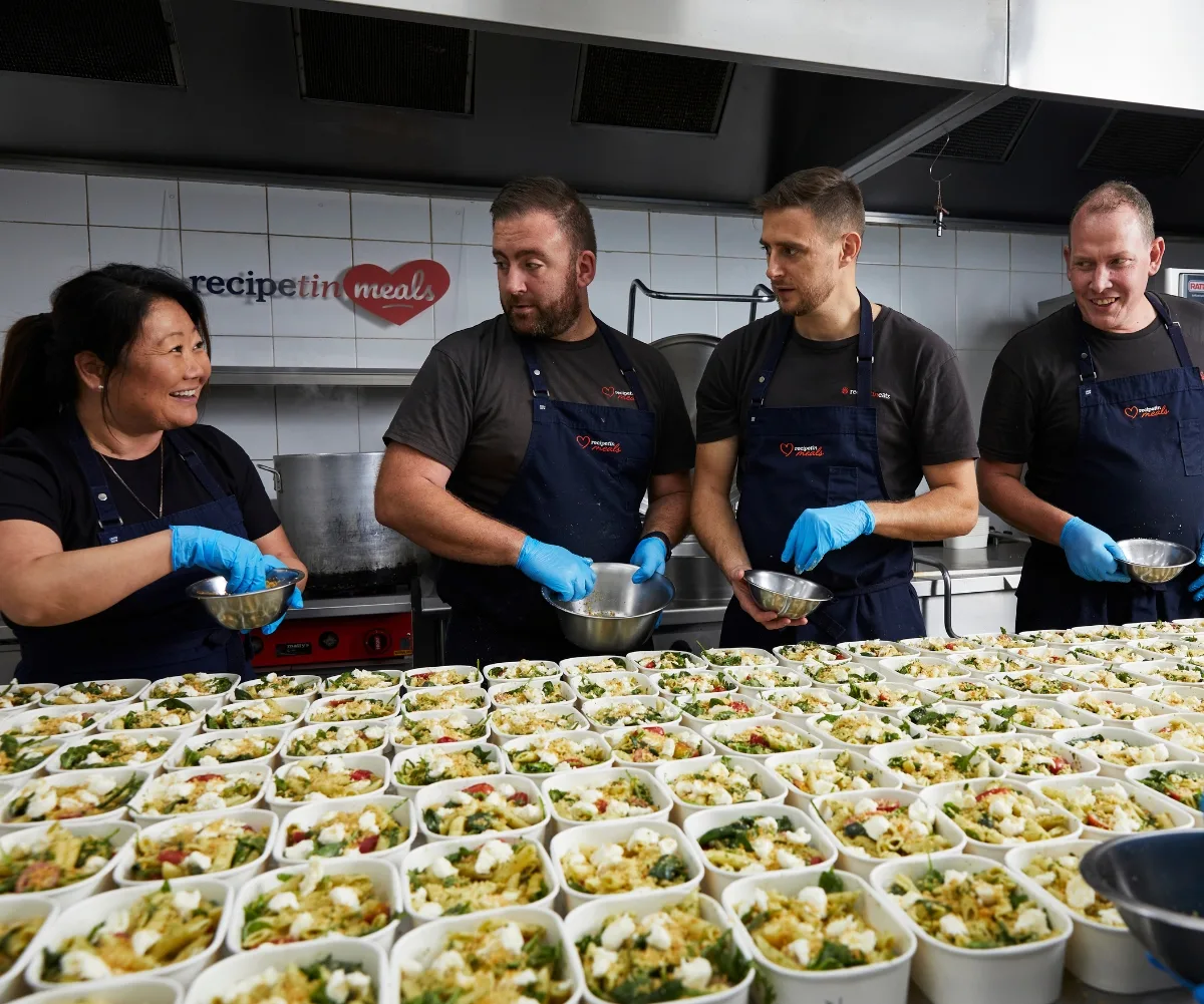 Nagi Maehashi standing in a kitchen with three other chefs, preparing food which is laid out in front of them.