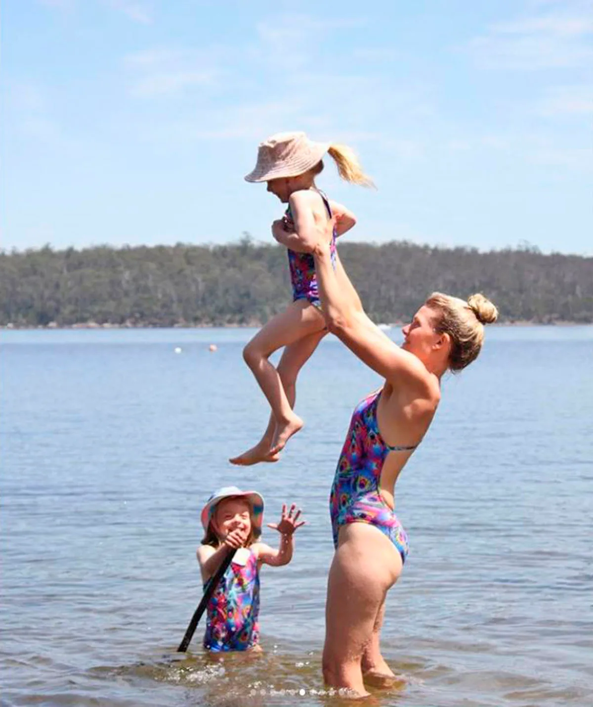 Bonnie Sveen, standing in a lake, lifts one of her twins in the air while the other one stands in the water. 