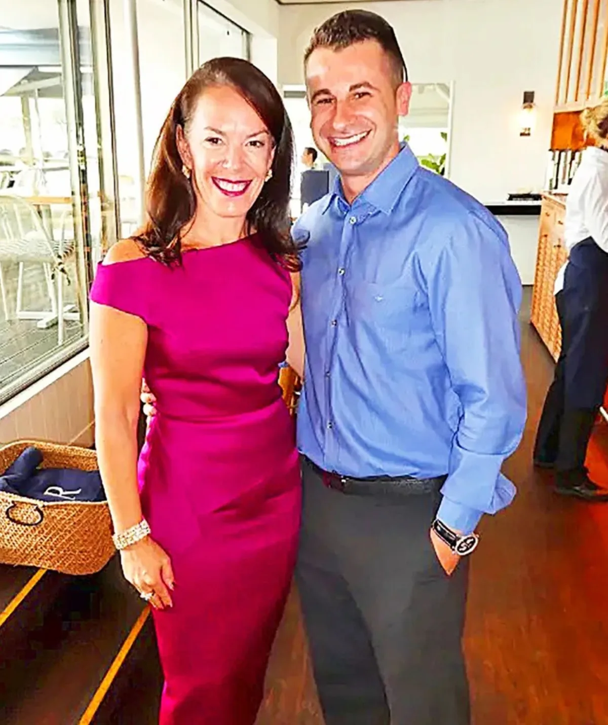 An image of Melissa Caddick and husband Anthony, smiling. She is wearing a pink dress, he is wearing dark trousers and a blue shirt.