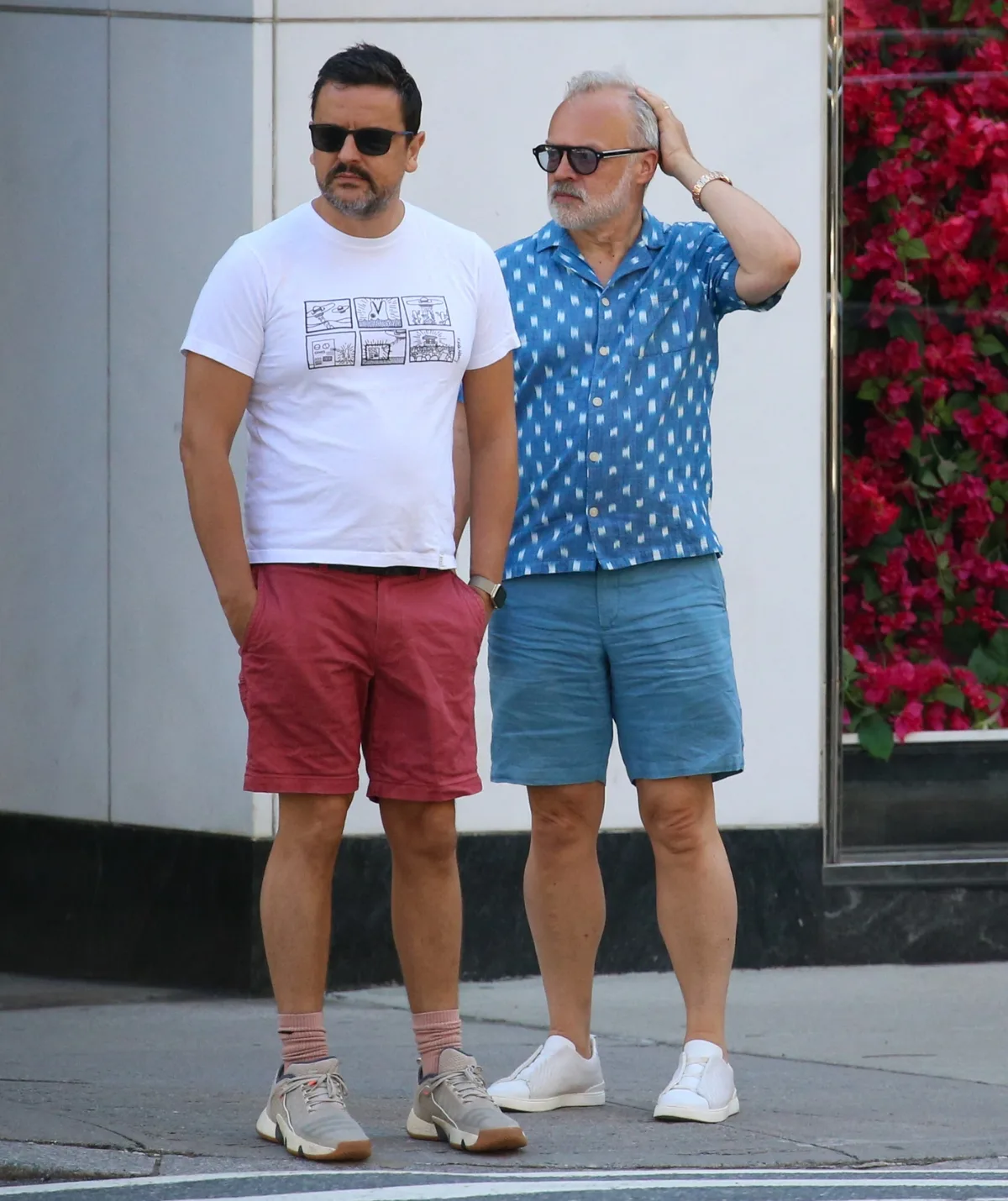 Graham Norton and his husband Jonathan McLeod are standing next to each other wearing shorts and t-shirts.