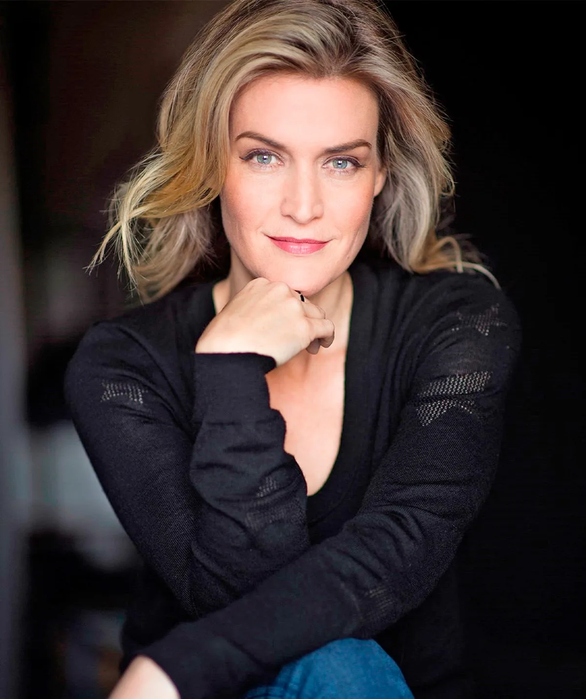 Jenni Baird, wearing a black top, poses with her hand on her chin.