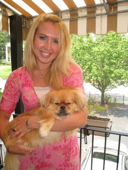 Blonde Lauren Giddings, who was murdered by Stephen McDaniel, in a pink dress holding her small golden dog, Butterbean, on a porch with a leafy tree in the background