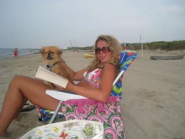 Blonde Lauren in pink bikini with her small golden dog sitting on a chair on a beach